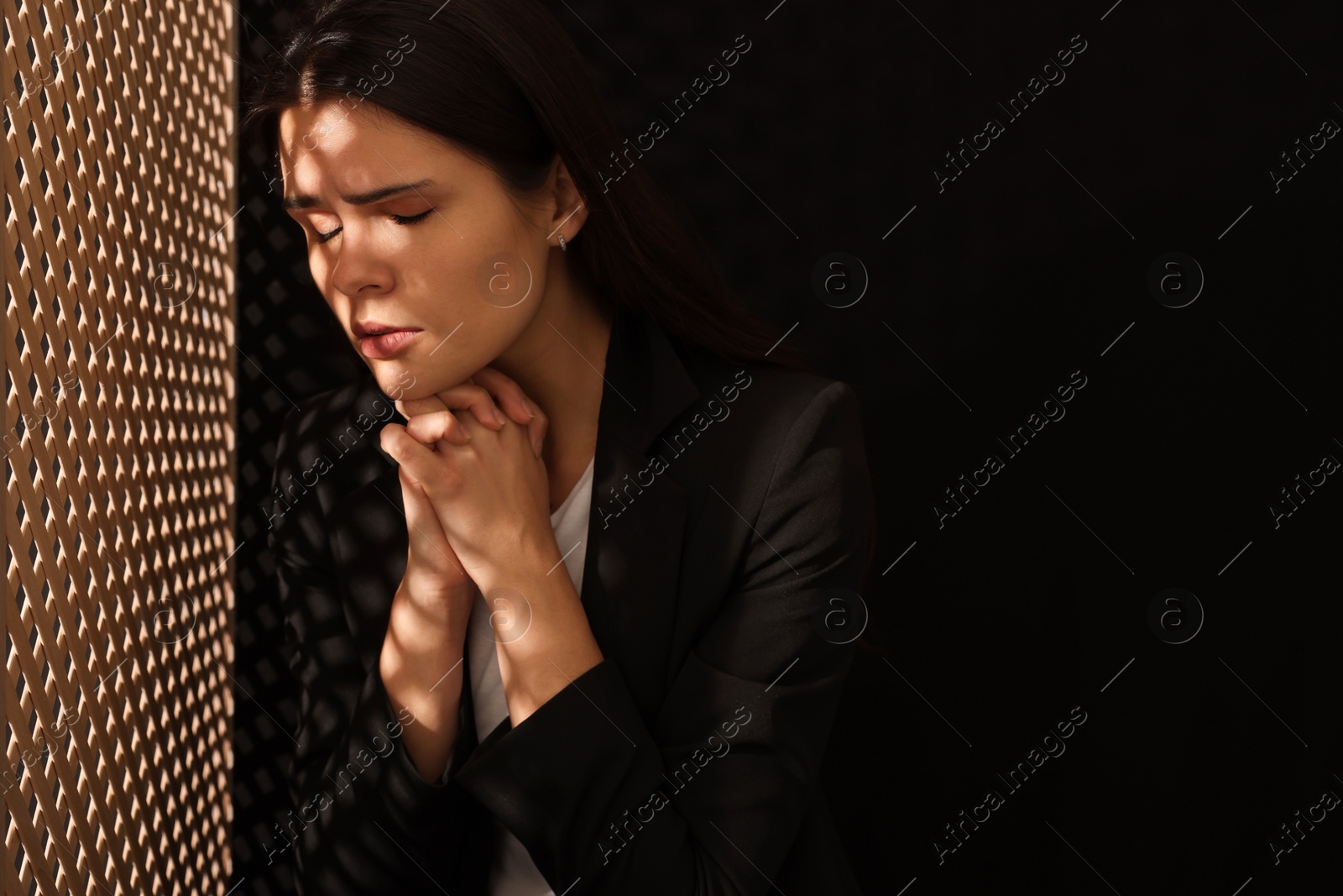 Photo of Woman praying to God during confession in booth, space for text