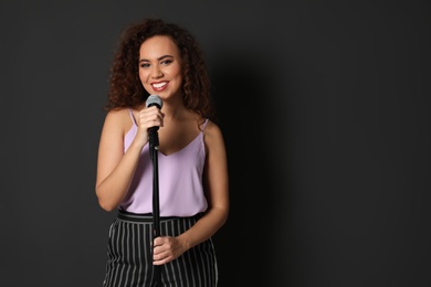 Curly African-American woman in stylish clothes posing with microphone on black background. Space for text