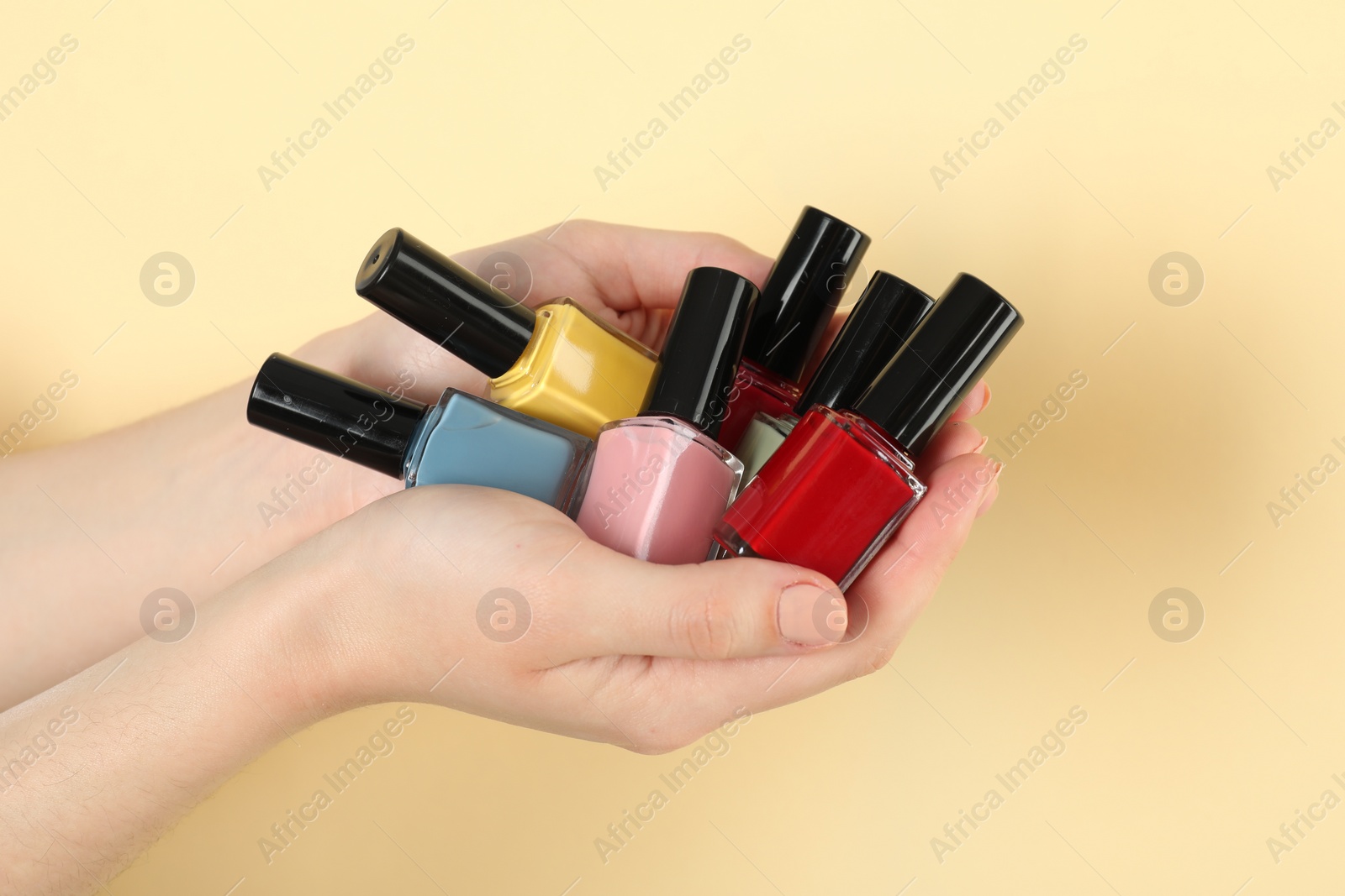 Photo of Woman holding nail polishes on beige background, closeup