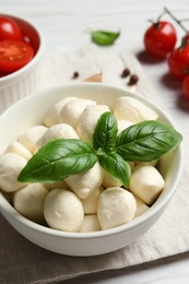 Delicious mozzarella balls and basil leaves in bowl on table, closeup