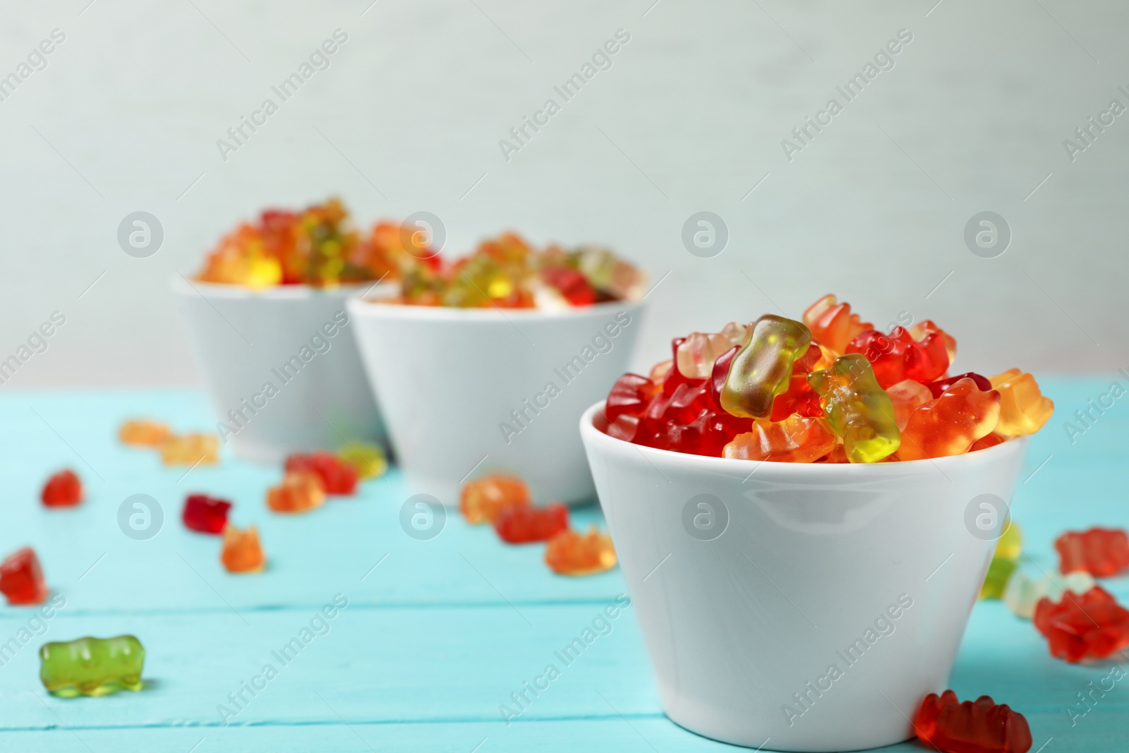 Photo of Bowls with delicious jelly bears on wooden table against light background. Space for text