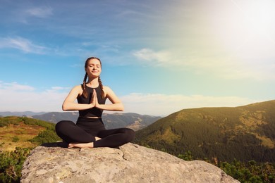 Image of Young woman practicing yoga in mountains on sunny morning