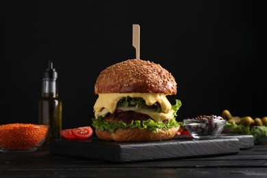 Photo of Vegetarian burger with delicious patty and cheese on black wooden table