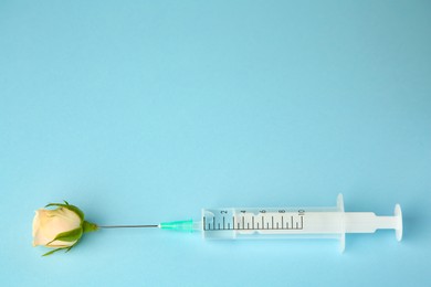 Photo of Medical syringe and beautiful rose on light blue background, top view. Space for text