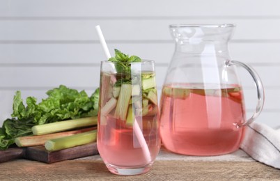 Tasty rhubarb cocktail and stems on wooden table