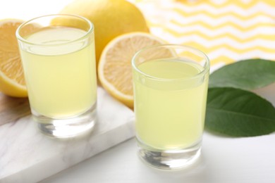Photo of Tasty limoncello liqueur, lemons and green leaves on white table, closeup