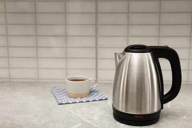 Photo of Modern electric kettle and cup of tea on grey marble kitchen counter. Space for text
