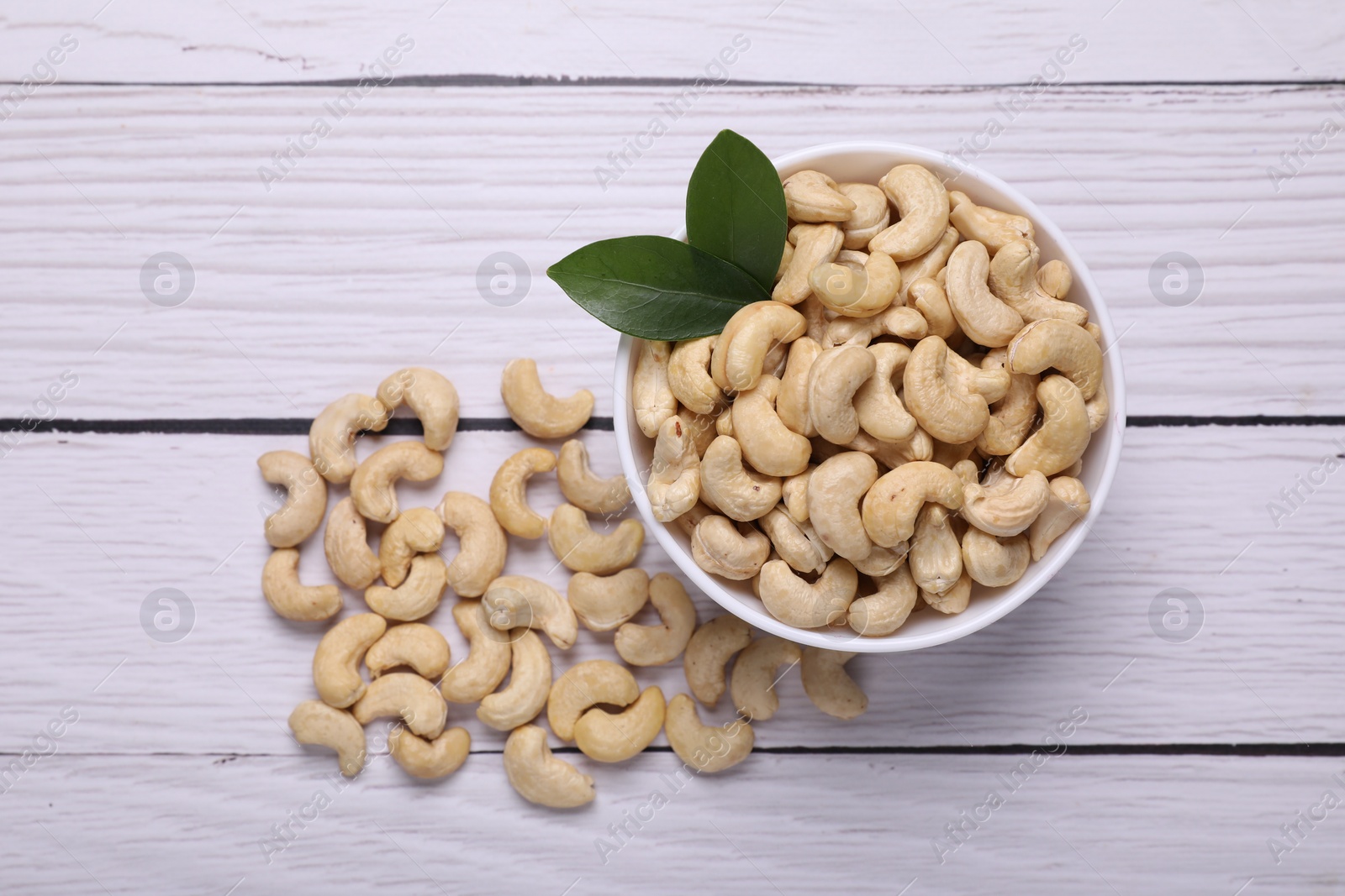 Photo of Tasty cashew nuts and green leaves on white wooden table, top view