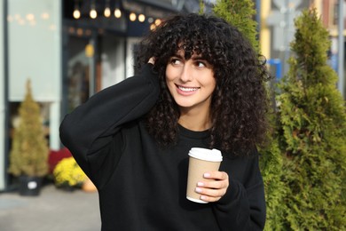 Happy young woman in stylish black sweater with cup of coffee outdoors