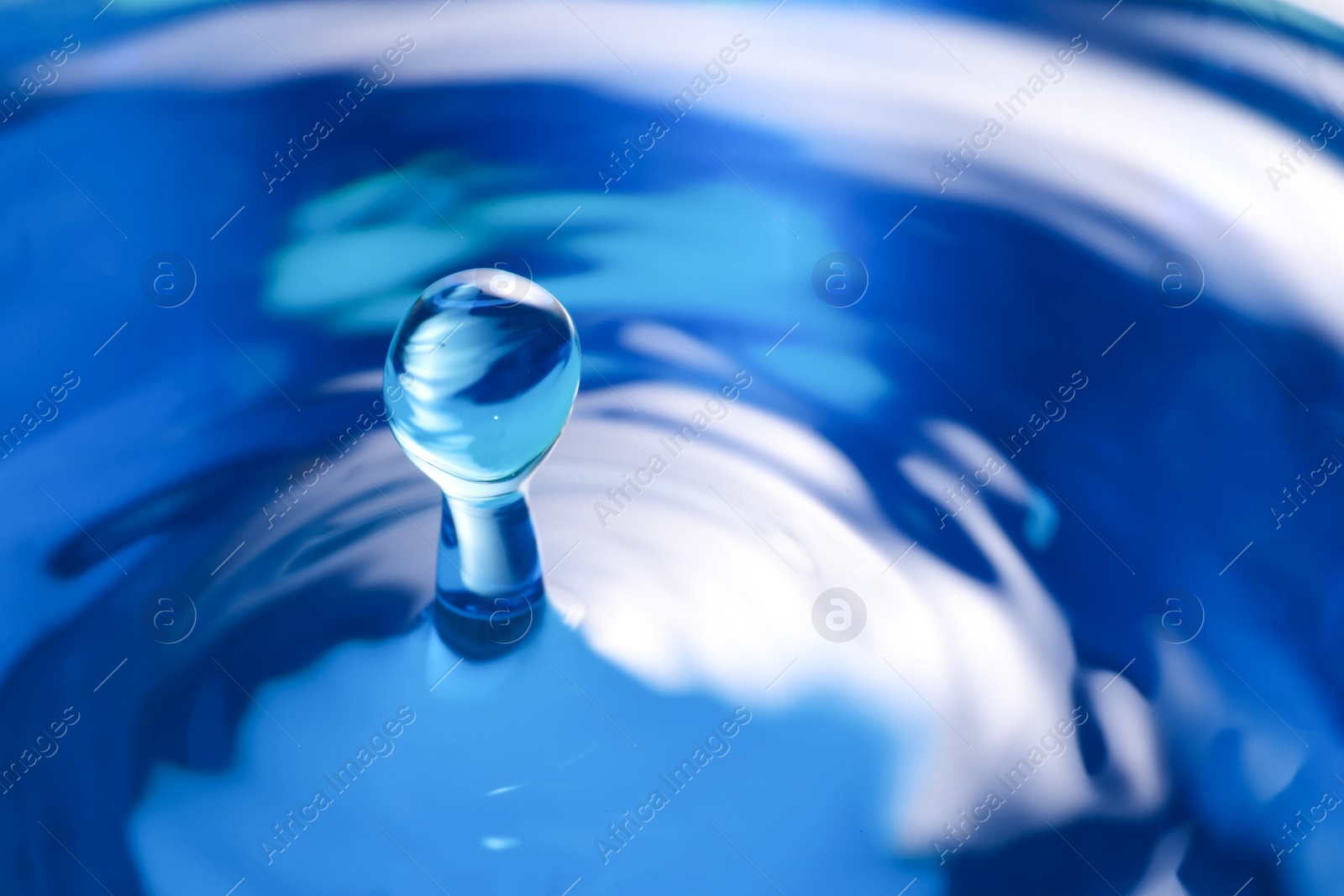 Photo of Drop falling into clear water on blue background, closeup