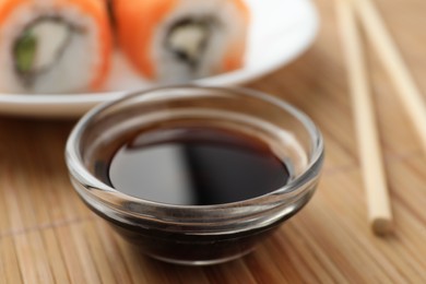 Bowl of tasty soy sauce on bamboo mat, closeup