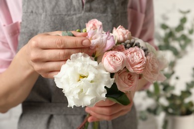 Photo of Florist creating beautiful bouquet with roses indoors, closeup