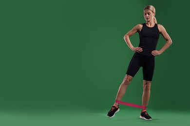 Photo of Athletic woman exercising with elastic resistance band on green background. Space for text