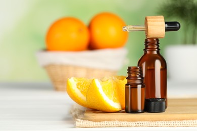 Photo of Bottles of essential oil, pipette and orange on white wooden table, space for text