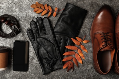 Photo of Flat lay composition with stylish black leather gloves, male shoes and dry leaves on grey table