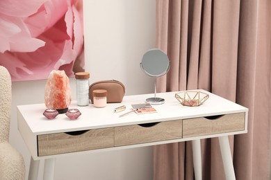 Photo of Dressing table with mirror, cosmetic products, jewelry and burning candles in makeup room