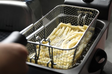 Photo of Chef cooking delicious french fries in hot oil, closeup