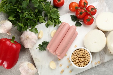 Photo of Fresh raw vegetarian sausages, soybeans and vegetables on grey table, flat lay