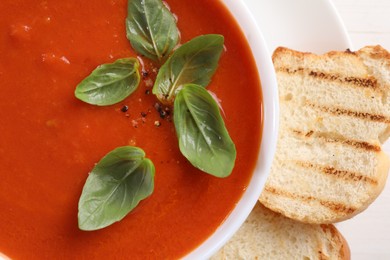 Photo of Delicious tomato cream soup in bowl with pieces of grilled bread on white table, top view