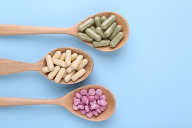 Different vitamin pills in wooden spoons on light blue background, flat lay. Space for text