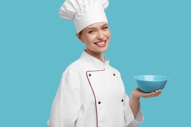 Photo of Happy chef in uniform holding bowl on light blue background