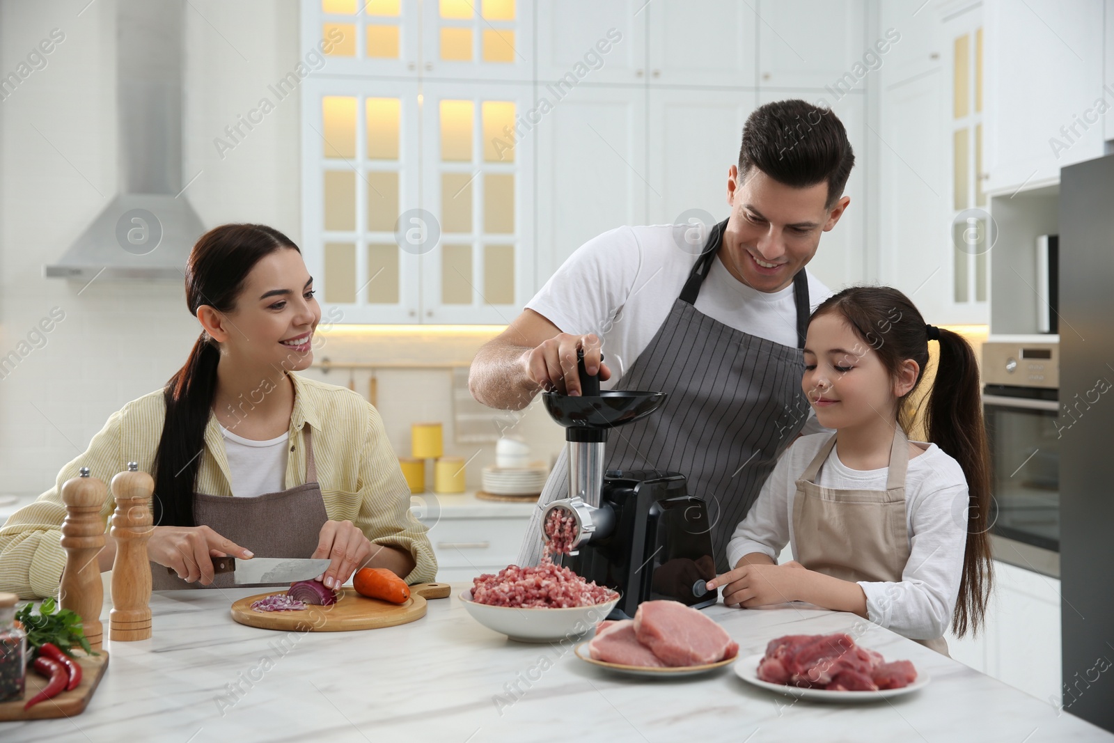 Photo of Happy family making dinner together in kitchen, father and daughter using modern meat grinder while mother cutting onion