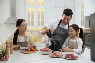 Photo of Happy family making dinner together in kitchen, father and daughter using modern meat grinder while mother cutting onion