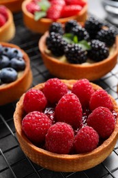 Photo of Tartlet with fresh raspberries on cooling rack, closeup. Delicious dessert