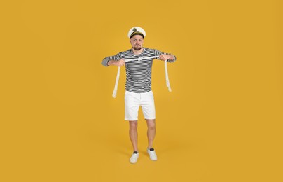 Photo of Serious sailor with rope on yellow background