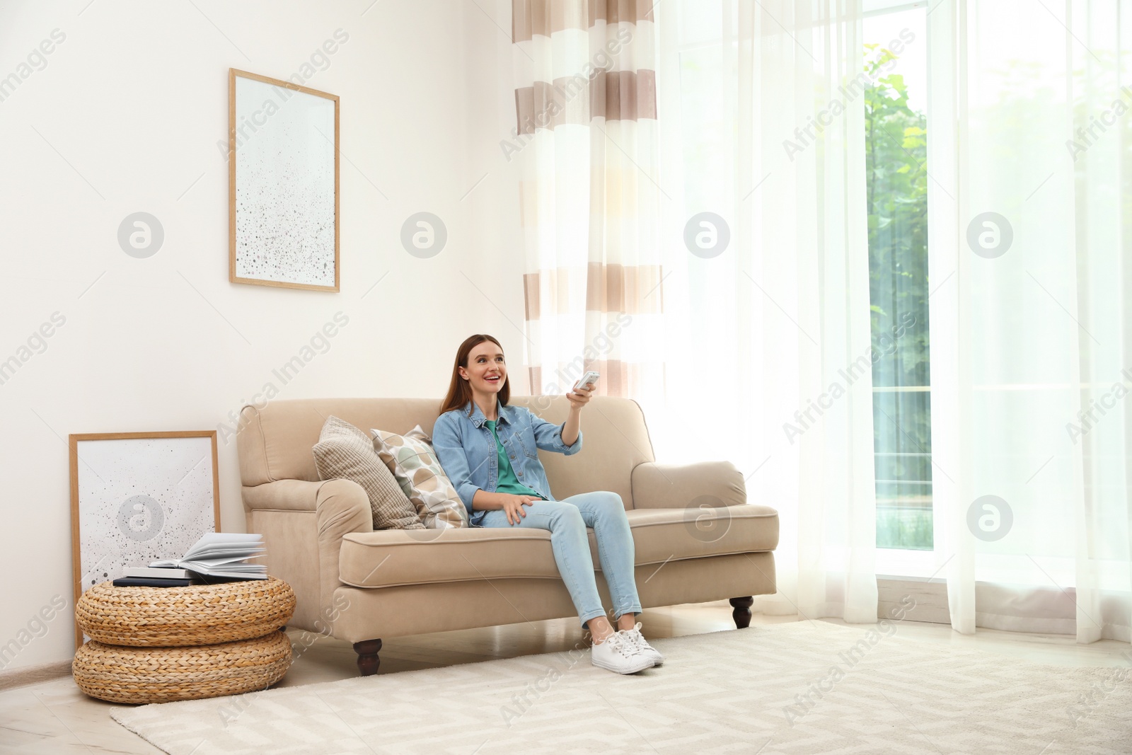 Photo of Happy young woman switching on air conditioner with remote control at home