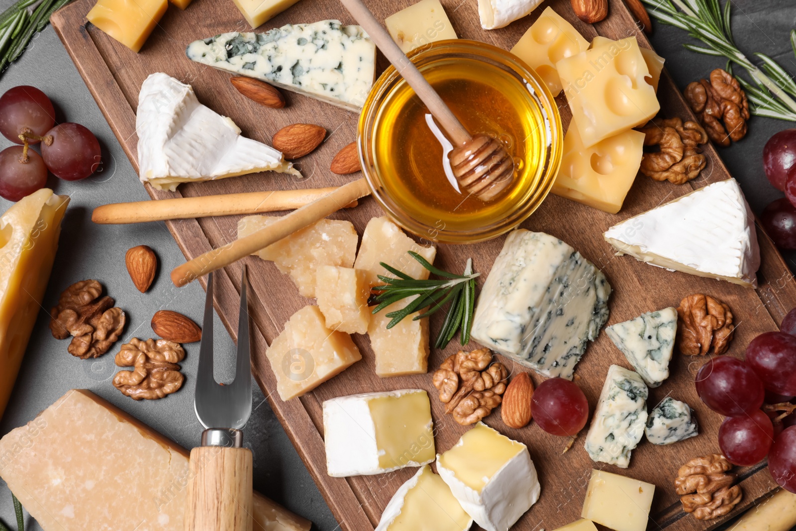 Photo of Cheese plate with honey, grapes and nuts on grey table, flat lay