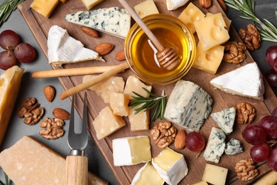 Cheese plate with honey, grapes and nuts on grey table, flat lay