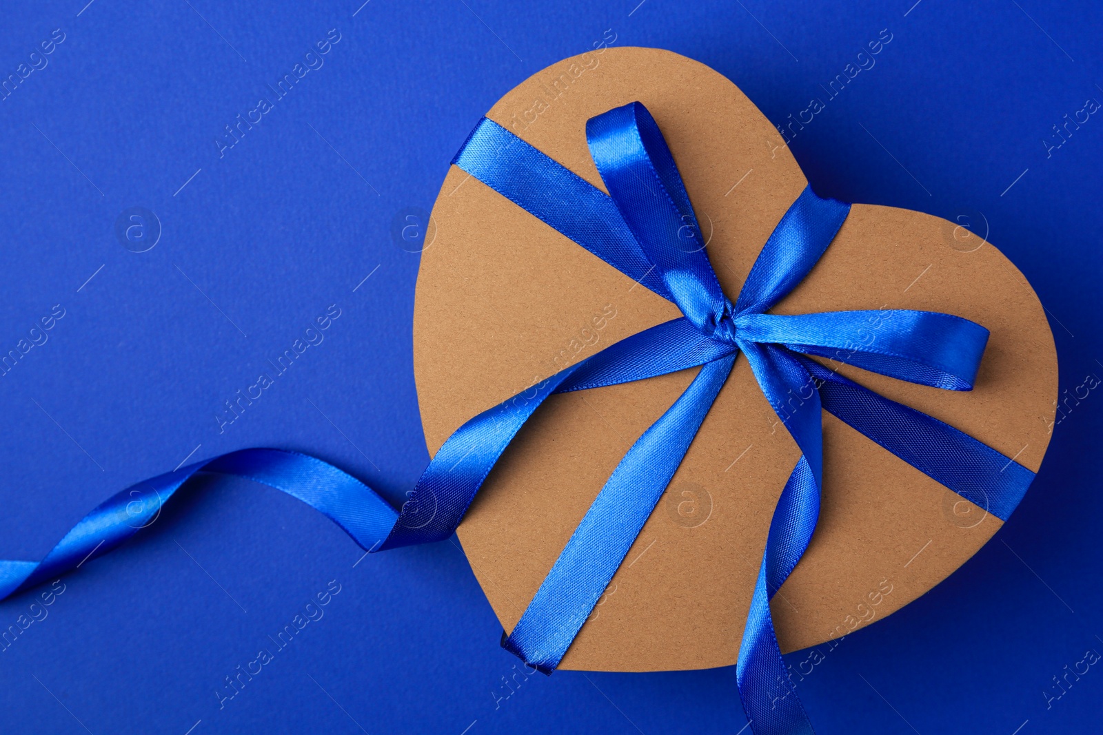 Photo of Beautiful heart shaped gift box with bow on blue background, top view