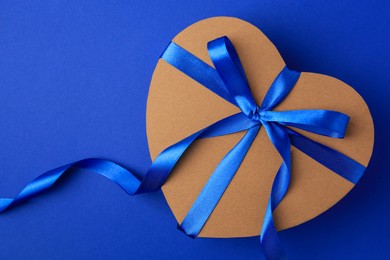 Beautiful heart shaped gift box with bow on blue background, top view