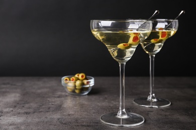 Photo of Glasses of Classic Dry Martini with olives on grey table against black background. Space for text
