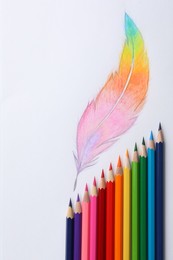 Drawing of feather and colorful pencils on white background, top view
