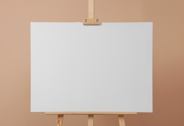 Wooden easel with blank canvas on beige background