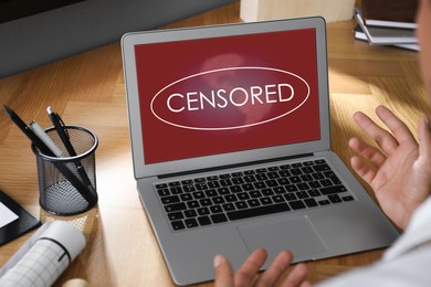 Image of Display with censorship sign. Man using laptop at wooden table, closeup