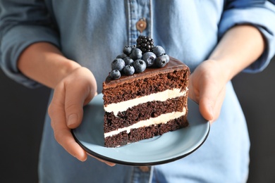 Photo of Woman holding plate with slice of chocolate sponge berry cake, closeup