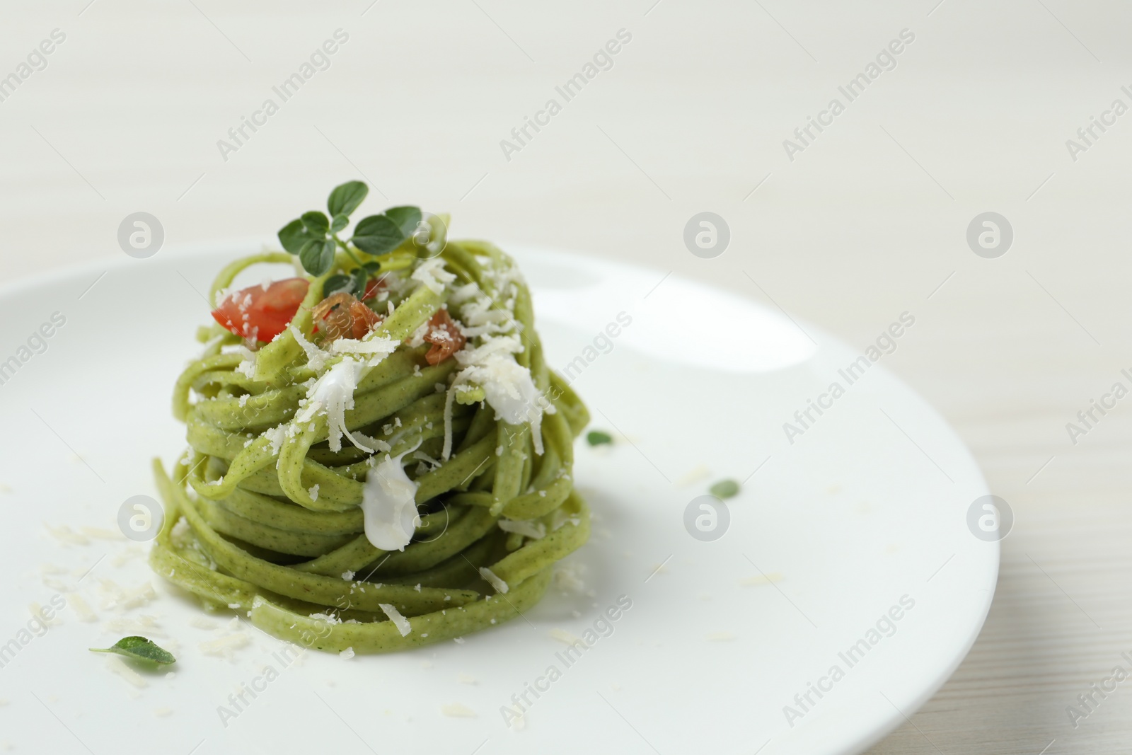 Photo of Tasty tagliatelle with spinach and cheese served on white wooden table, closeup. Exquisite presentation of pasta dish