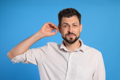 Photo of Emotional man cleaning ears on light blue background