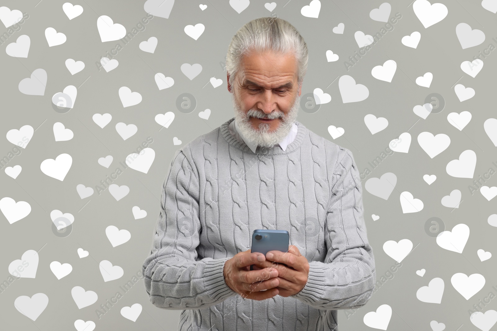 Image of Long distance love. Man chatting with sweetheart via smartphone on grey background. Hearts around him