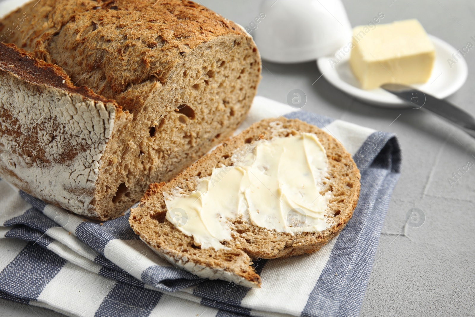 Photo of Slice of tasty bread with butter near loaf on grey table