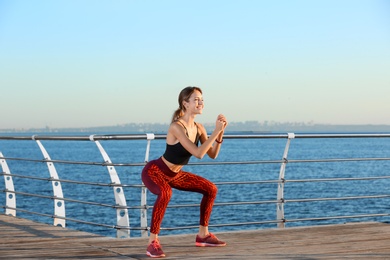 Photo of Young woman doing fitness exercises on pier in morning