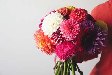 Woman with bouquet of beautiful dahlia flowers on light background, closeup. Space for text