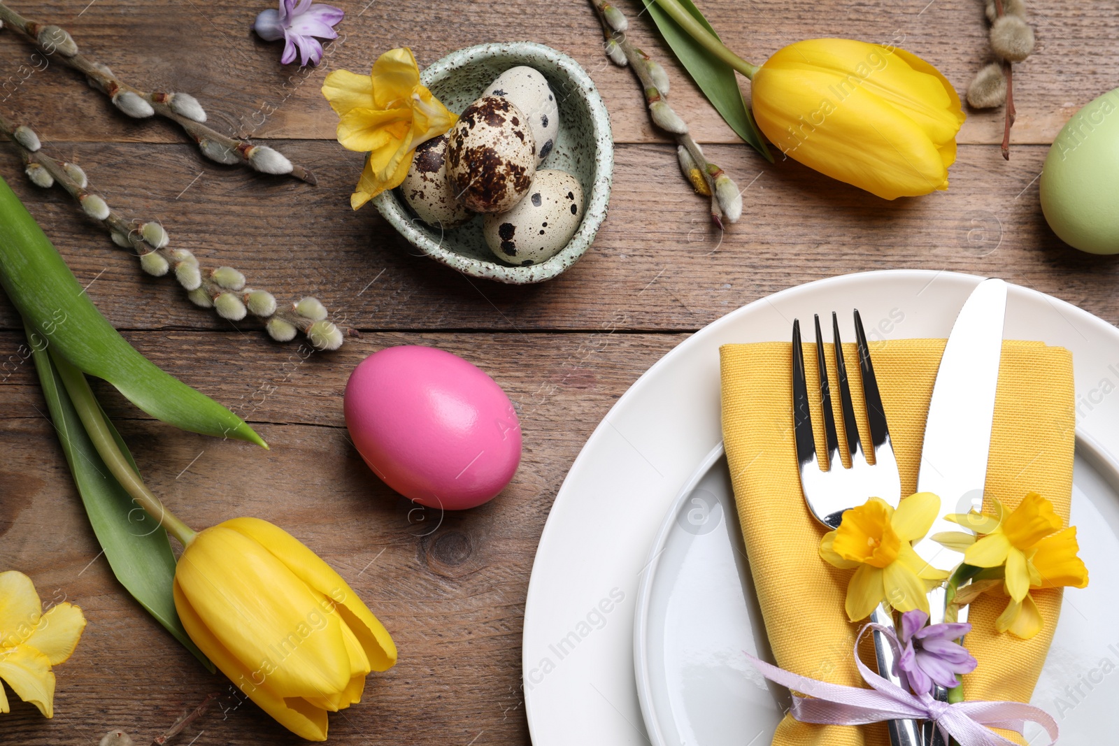 Photo of Festive Easter table setting with painted eggs and floral decor on wooden background, flat lay