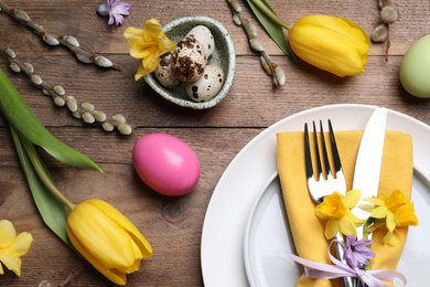 Festive Easter table setting with painted eggs and floral decor on wooden background, flat lay