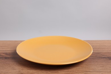 Photo of Empty ceramic plate on wooden table against light background, space for text