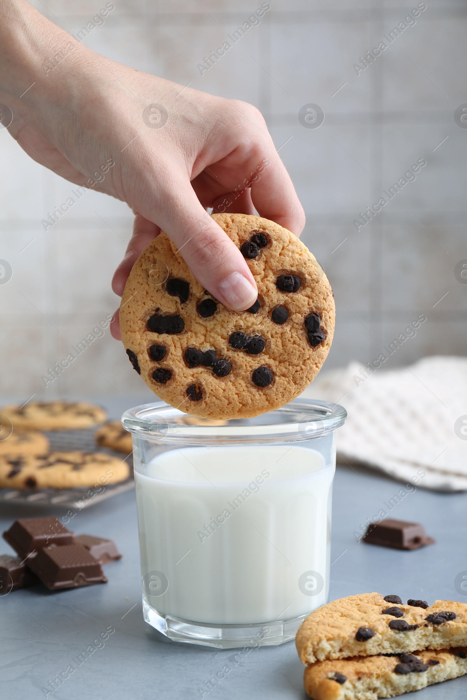 Woman dipping delicious chocolate chip cookie into glass of milk at grey table, closeup Photo of Woman dipping delicious chocolate chip cookie into glass of milk at grey table, closeup
