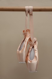 Photo of Elegant pointes hanging on ballet barre against beige background